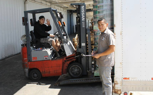 Warehouse workers using a forklift to load containers into a delivery truck.
