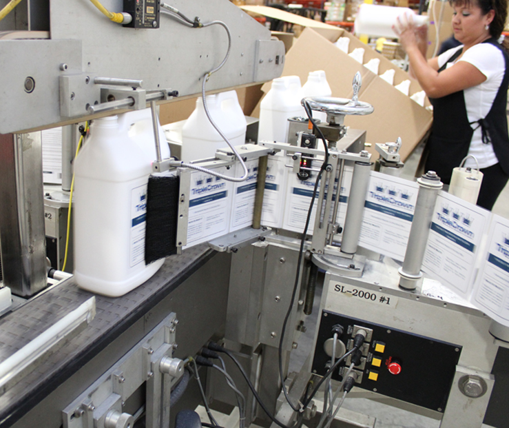 A processing plant showing automated machine attaching labels to a packaging container.